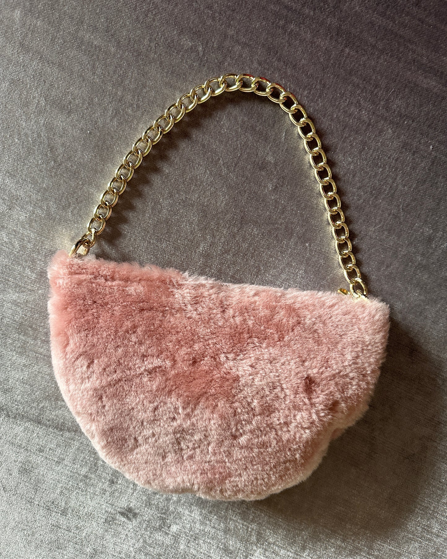 Pink shearling half moon shaped bag with two metal hardware details and metal chain strap.