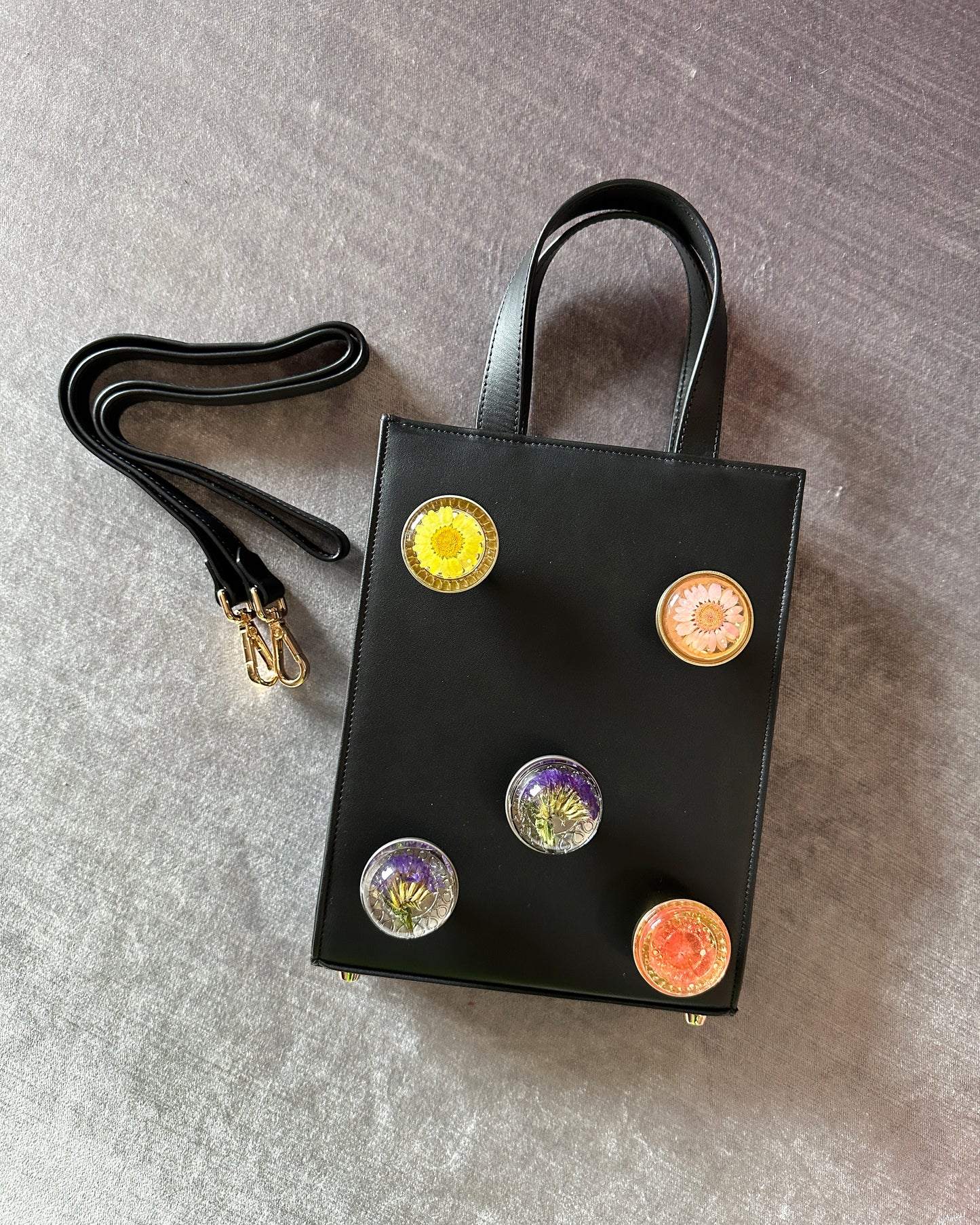 Black leather bag with 5 assorted preserved  floral knobs.