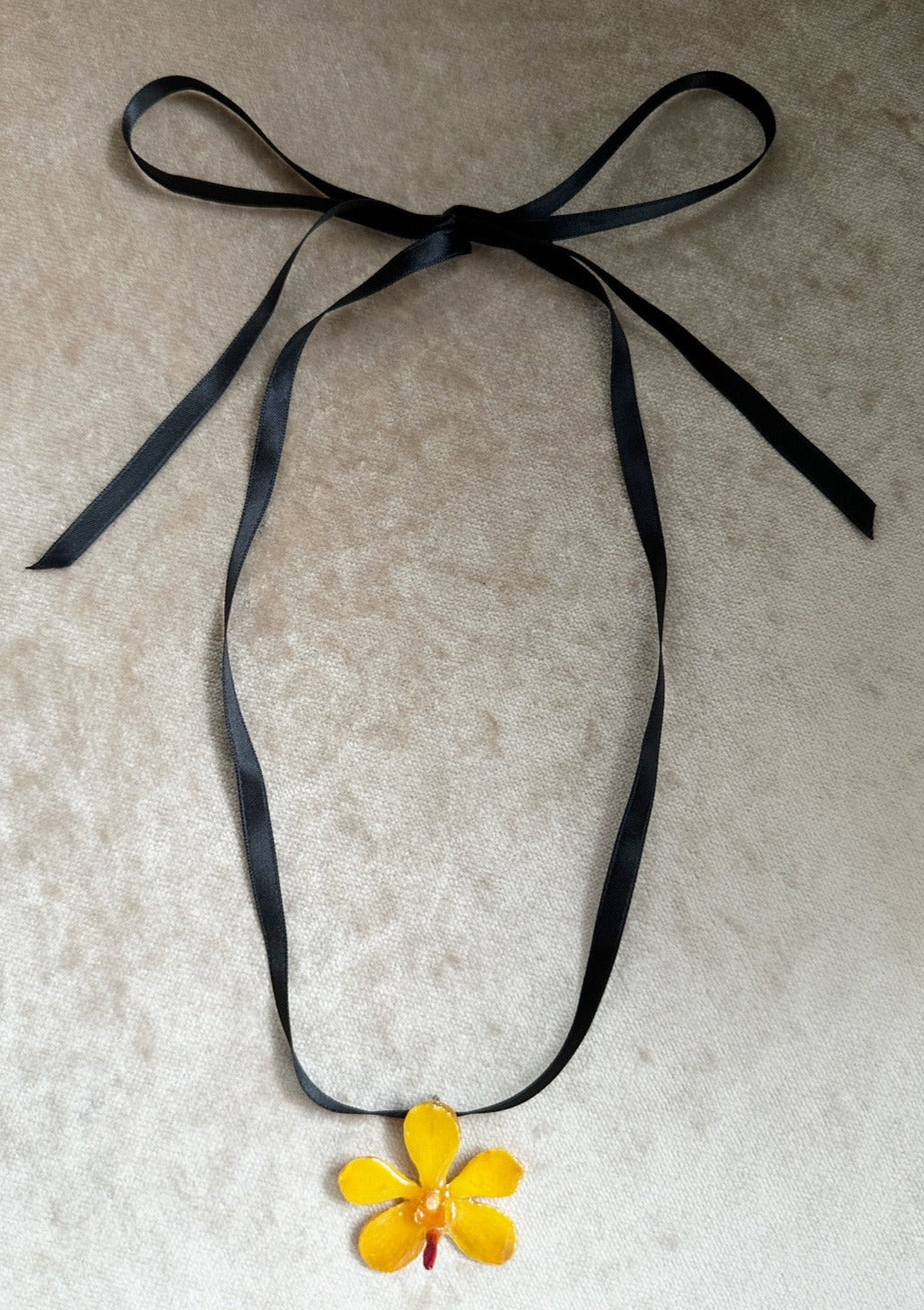 Sunshine Mokara orchid preserved in resin and suspended from a black satin ribbon.
