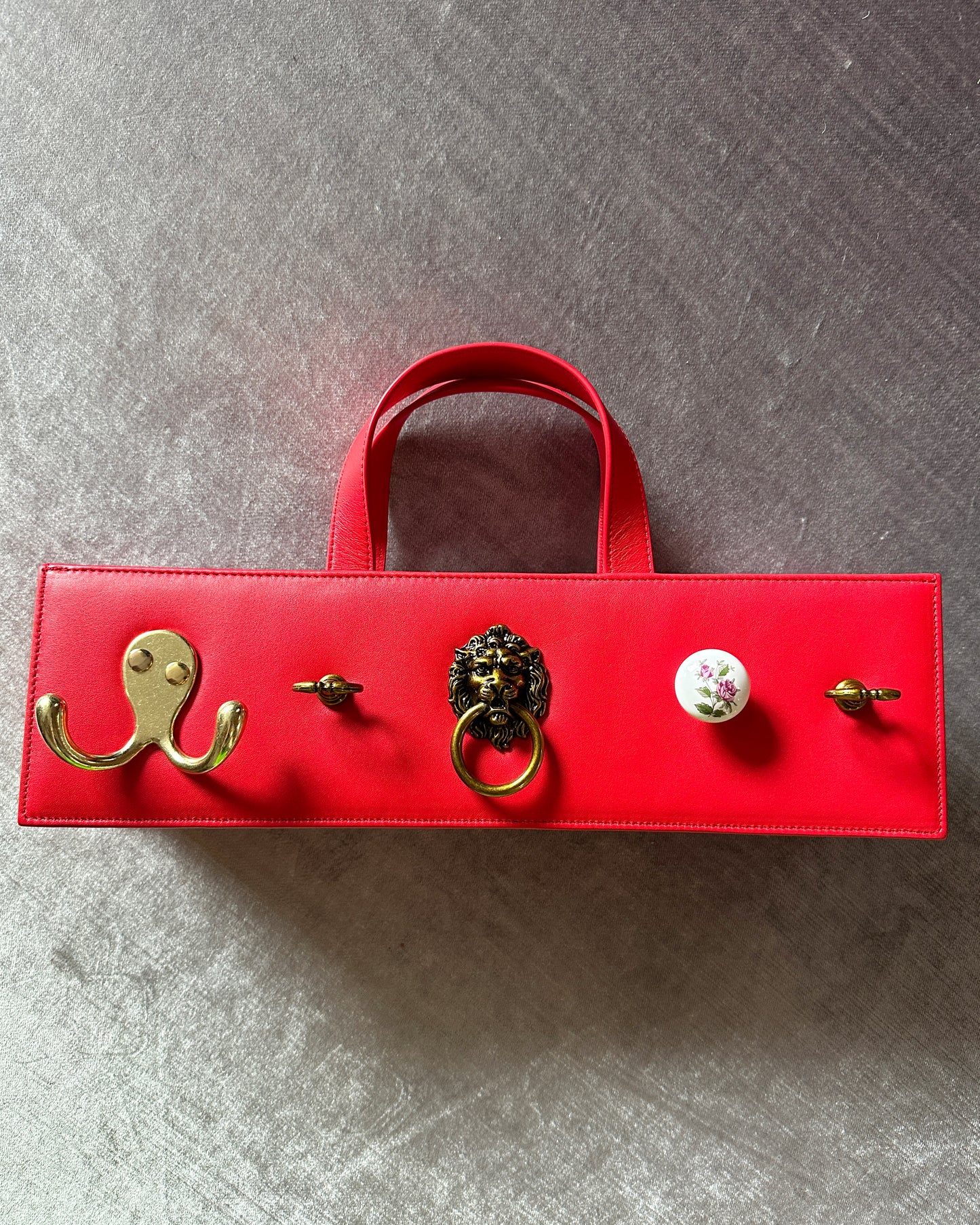 Rectangular cherry red leather bag with five assorted metal and ceramic hardware embellishments. 