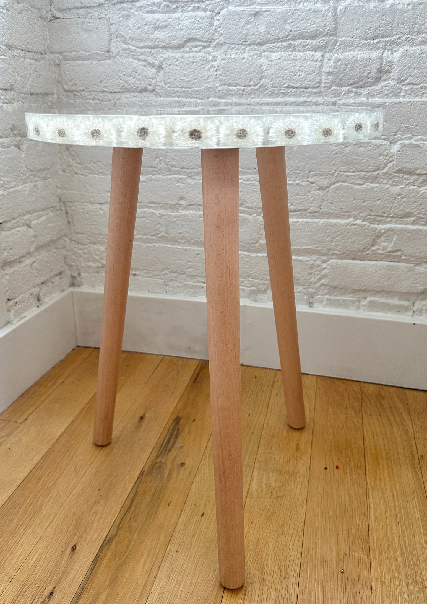 a hand-poured resin desk where dozens of dandelions float atop three wooden legs.