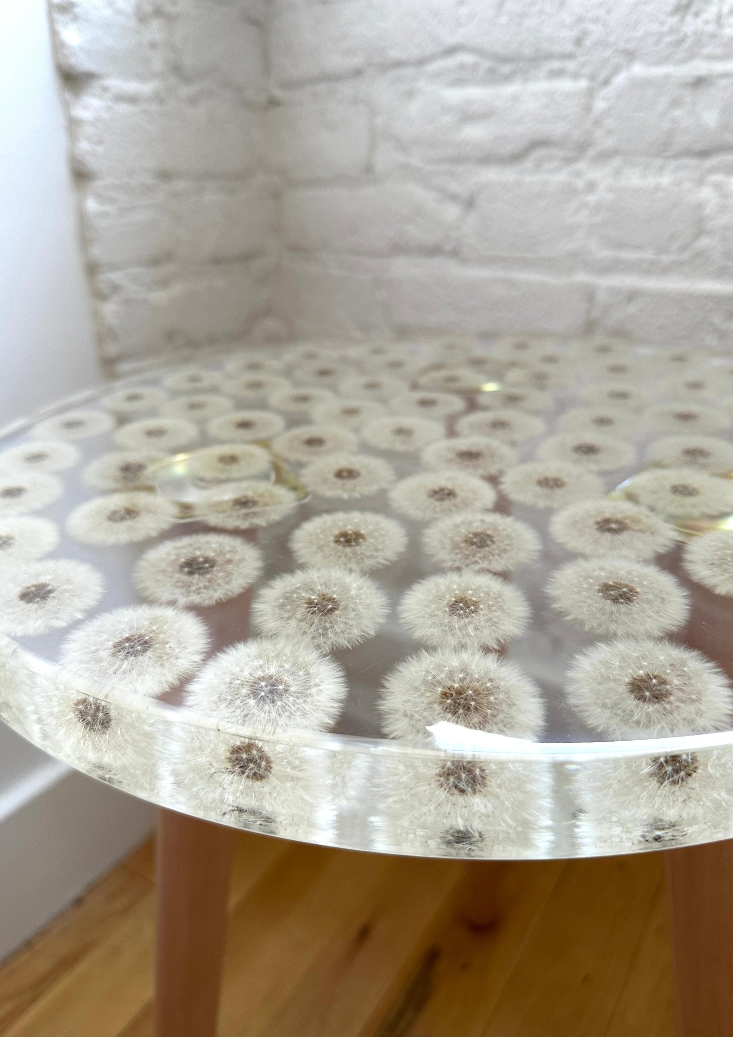 a hand-poured resin desk where dozens of dandelions float atop three wooden legs.
