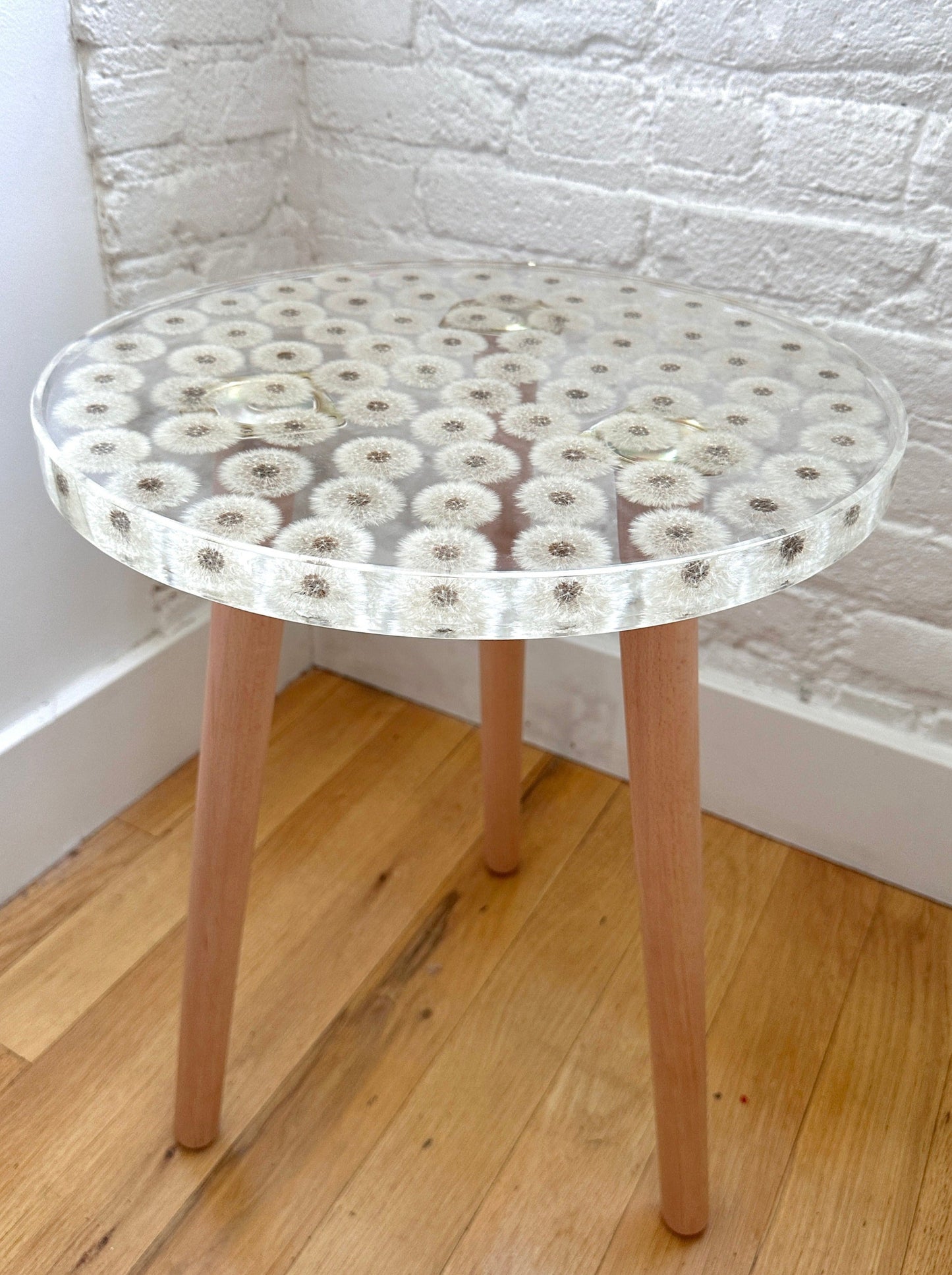 a hand-poured resin desk where dozens of dandelions float atop three wooden legs.