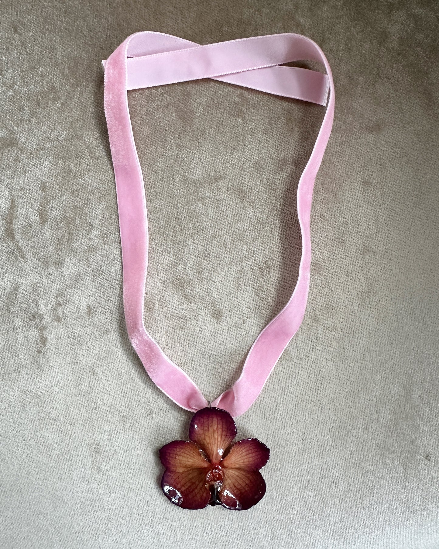 Black and pink orchid preserved in resin suspended from pink velvet ribbon.