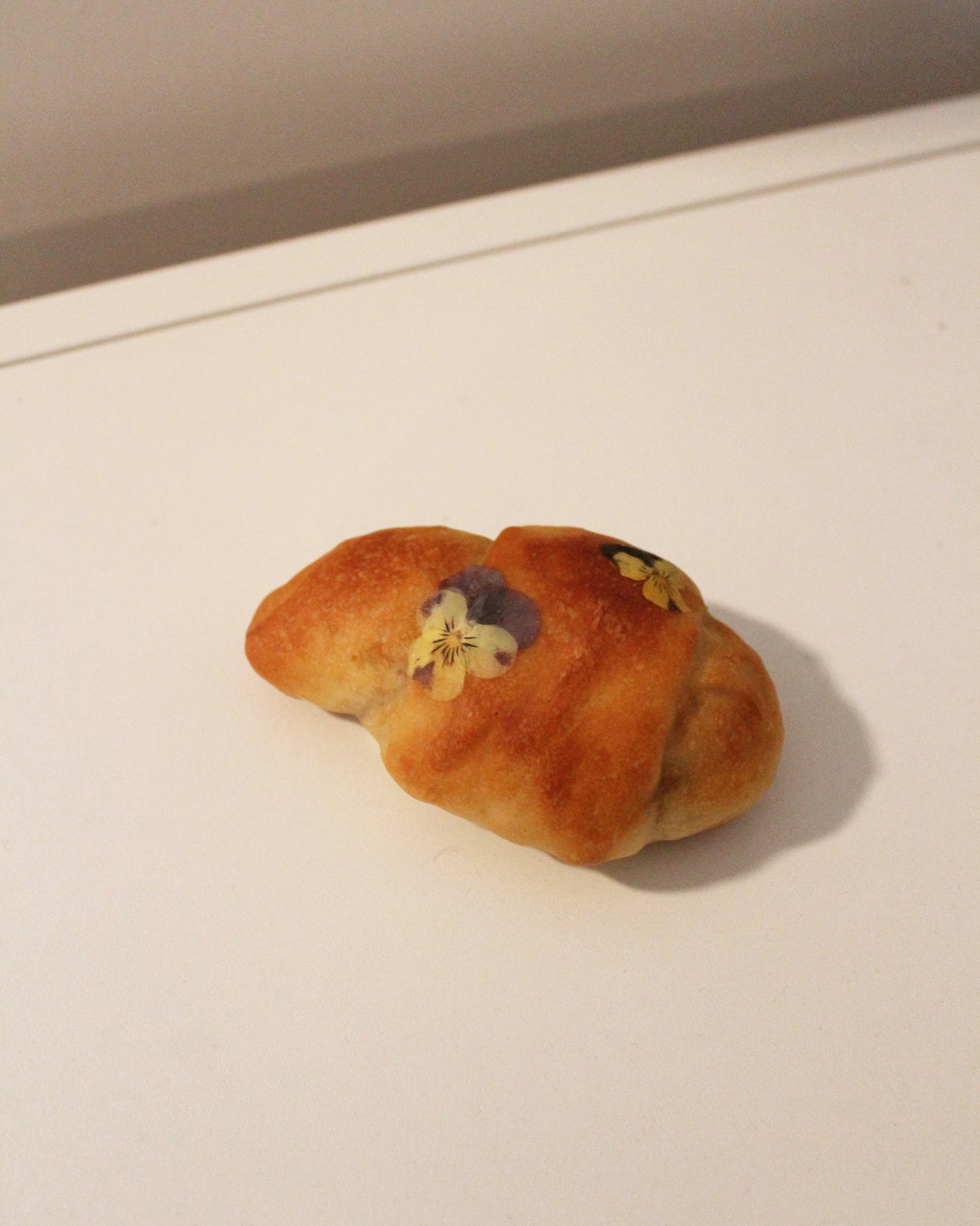 A mini bread roll lamp with daisies adorning it. Crafted from real, surplus bread that would otherwise be discarded-- baked, hollowed, and reimagined into a delightful lamp in Japan. Coated in an anti-bacterial and anti-fungal, eco-friendly resin.
