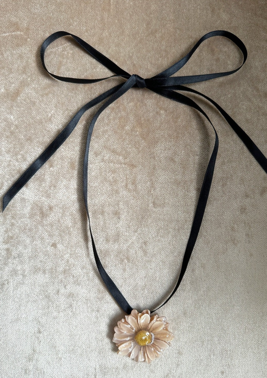 Ivory daisy pendant diped in resin suspended from a black satin ribbon.
