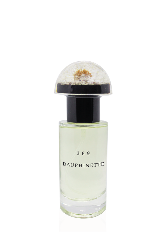A clear glass cylindrical bottle of Dauphinette's signature perfume labeled "369 Dauphinette" with a resin dandelion "mushroom cap" bottle topper.