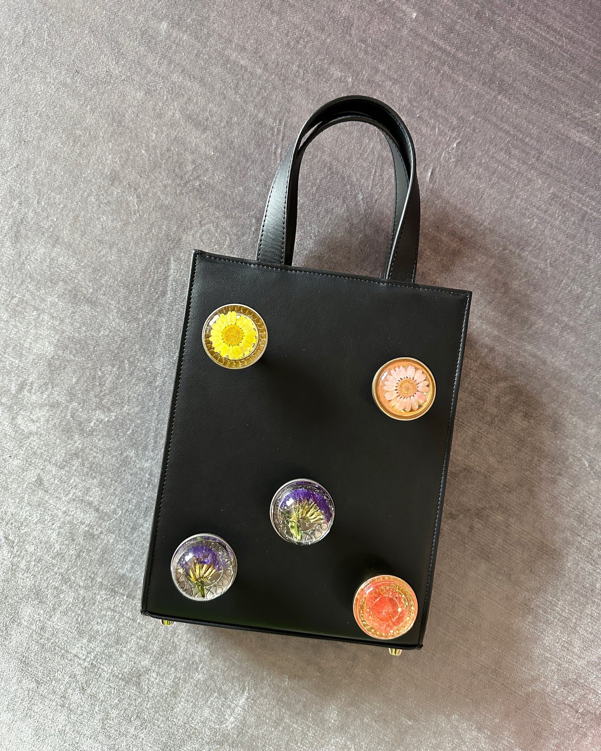 Black leather bag with 5 assorted preserved  floral knobs.