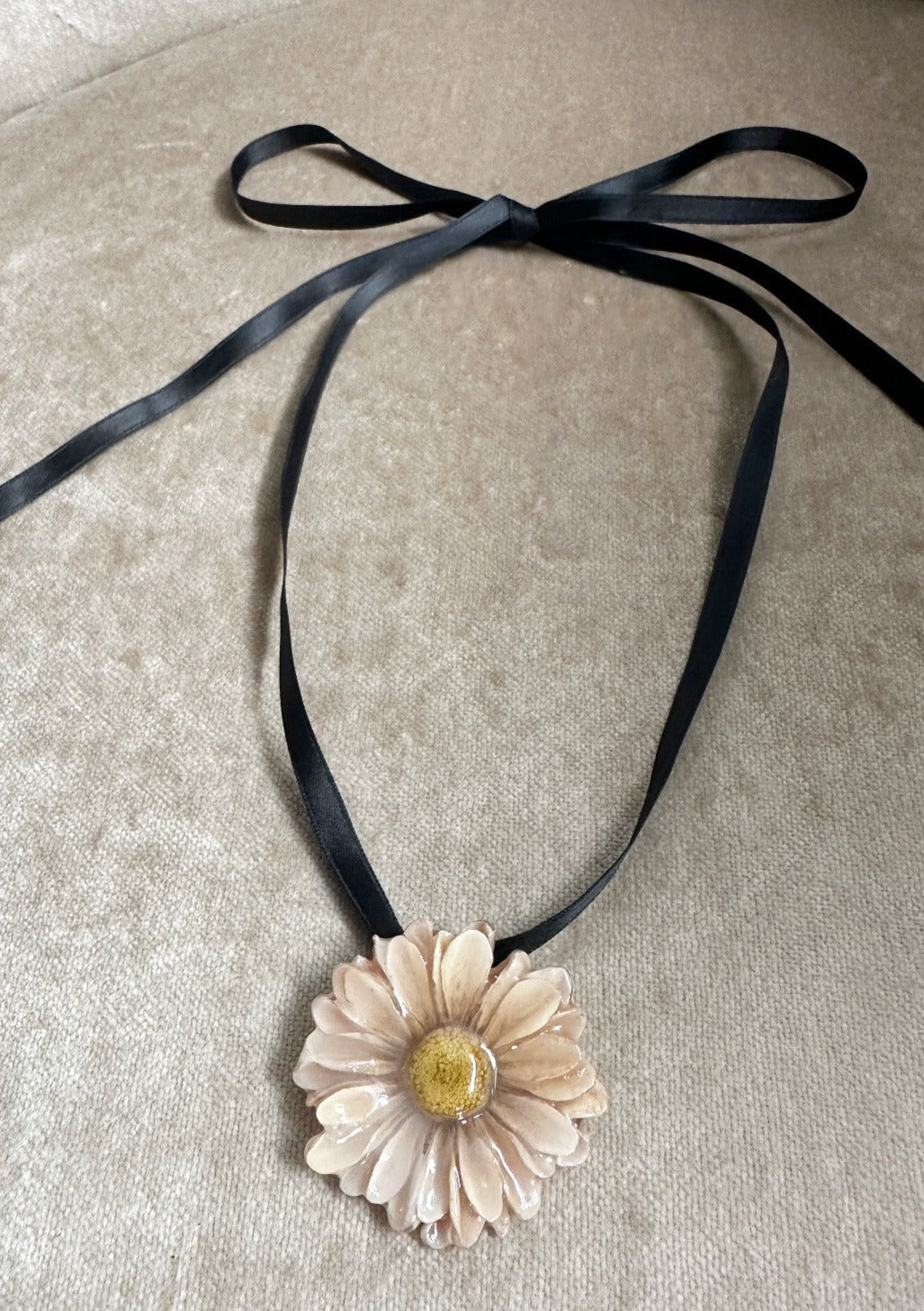 Ivory daisy pendant diped in resin suspended from a black satin ribbon.