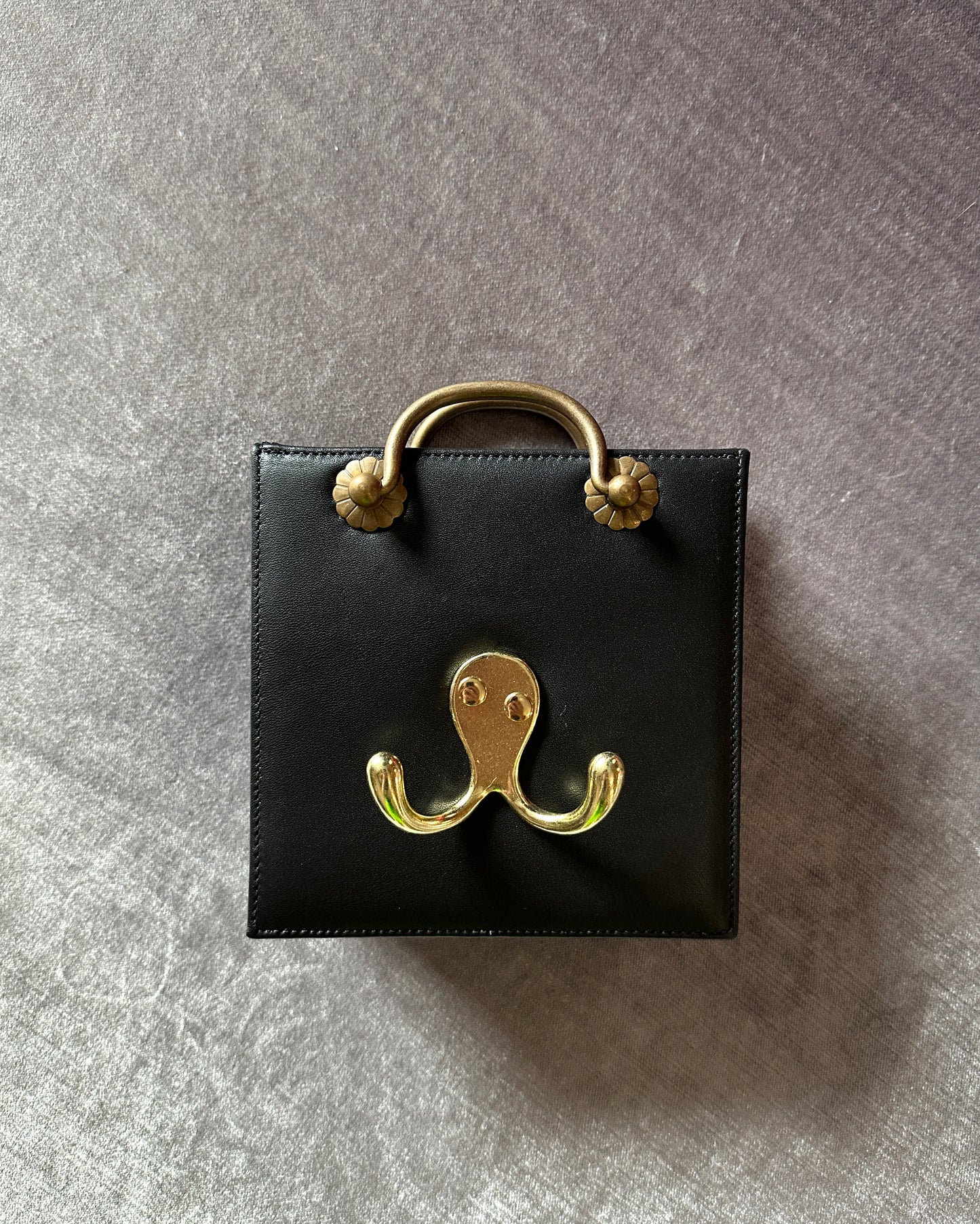 Mini black leather bag with gold handle and hanger hardware.