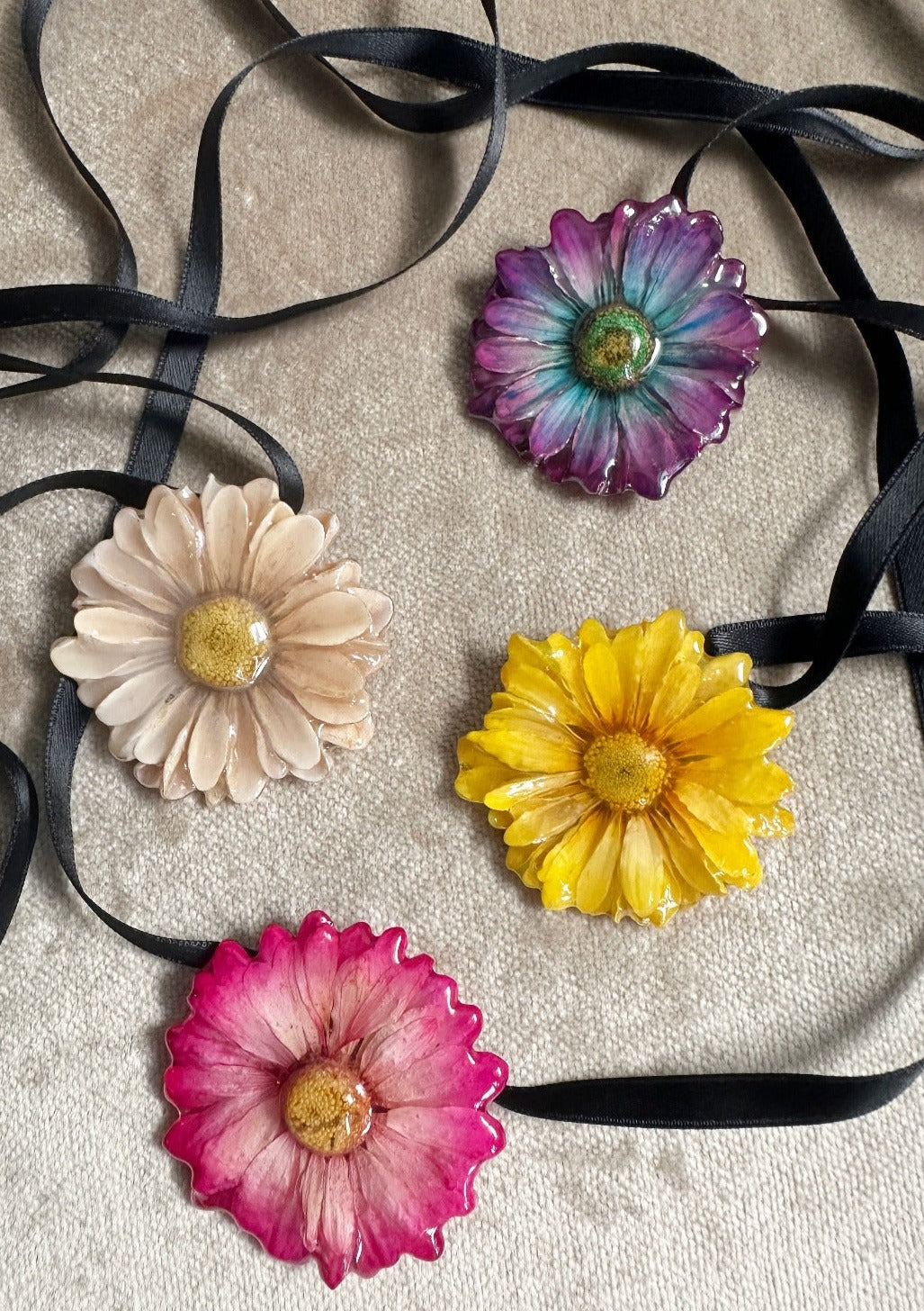 Assorted daisies preserved in resin and suspended from black satin ribbons.