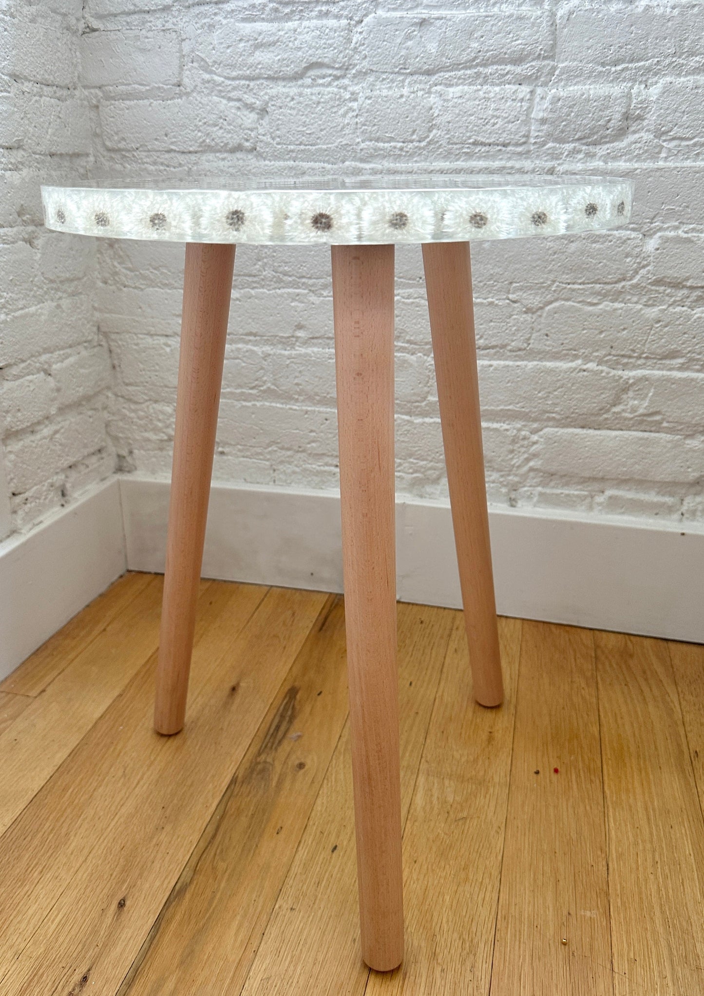 a hand-poured resin desk where dozens of dandelions float atop three wooden legs.
