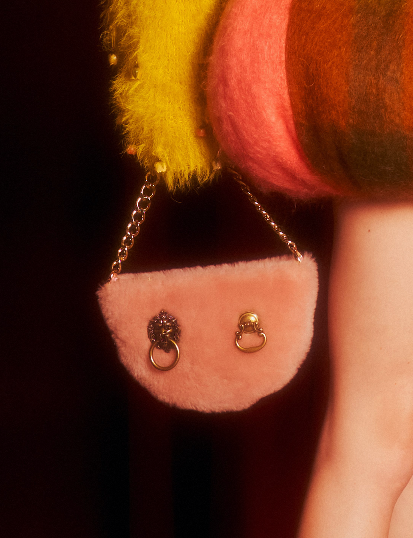 Pink shearling half moon shaped bag with two metal hardware details and metal chain strap.