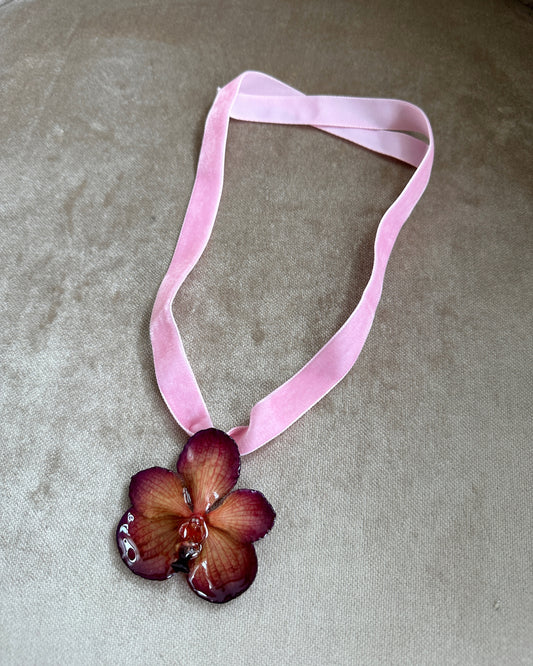 Black and pink orchid preserved in resin suspended from pink velvet ribbon.