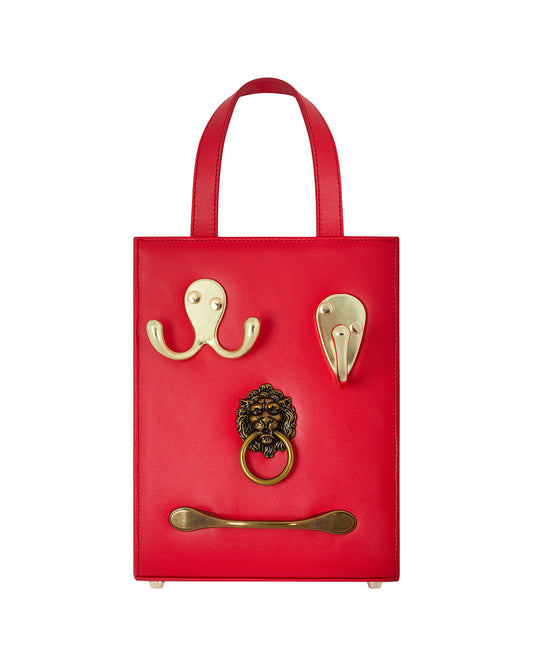 Cherry leather upper bag with 4 gold metal hardware sorted hangers, handles, and door knockers attached to the front of the bag.