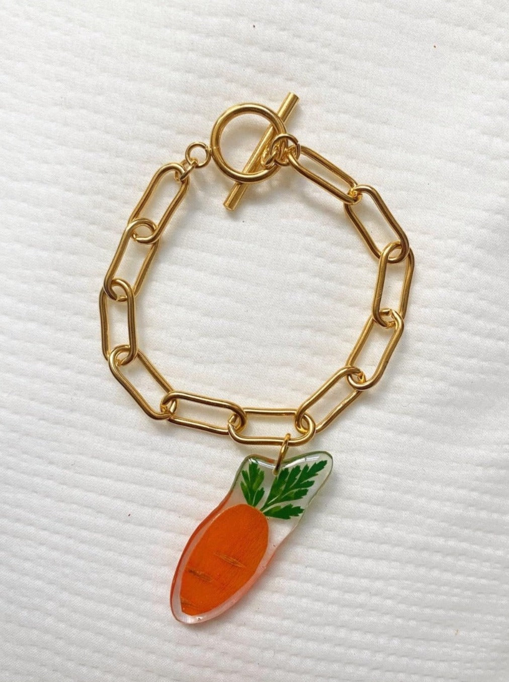 Tiny baby carrot slice suspended from a gold-plated stainless steel Albert chain.