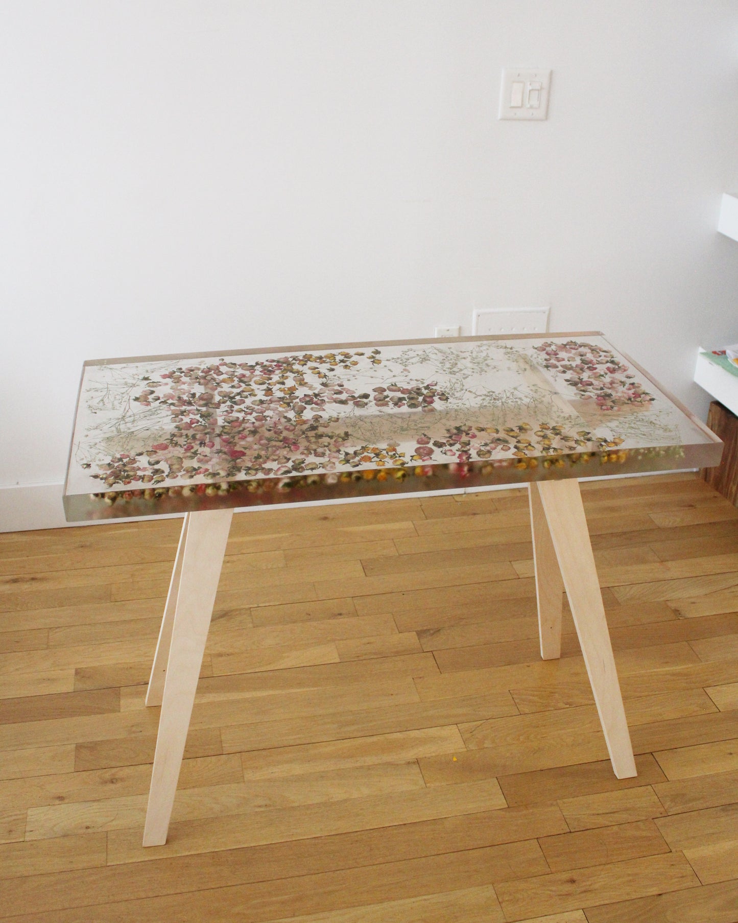 a hand-poured resin desk where hundreds of real rosebuds and baby's breath sprigs float atop a sturdy birch base