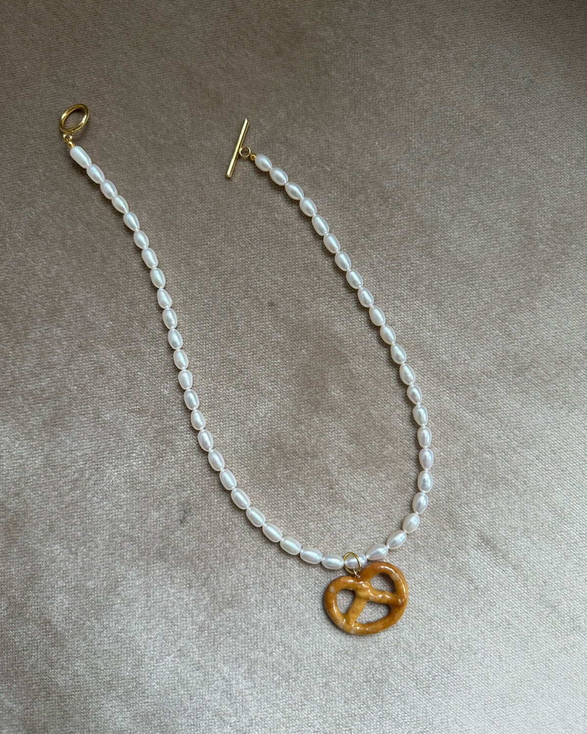 Resin coated pretzel on beaded pearl necklace with gold clasp.