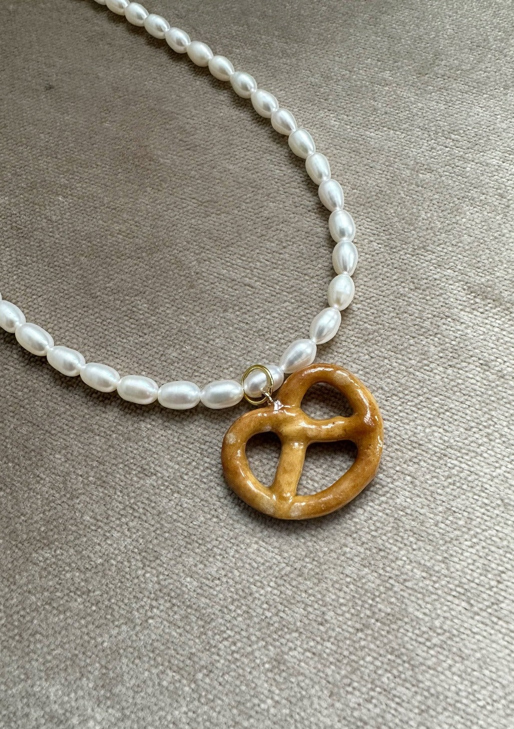 Resin coated pretzel on beaded pearl necklace with gold clasp.