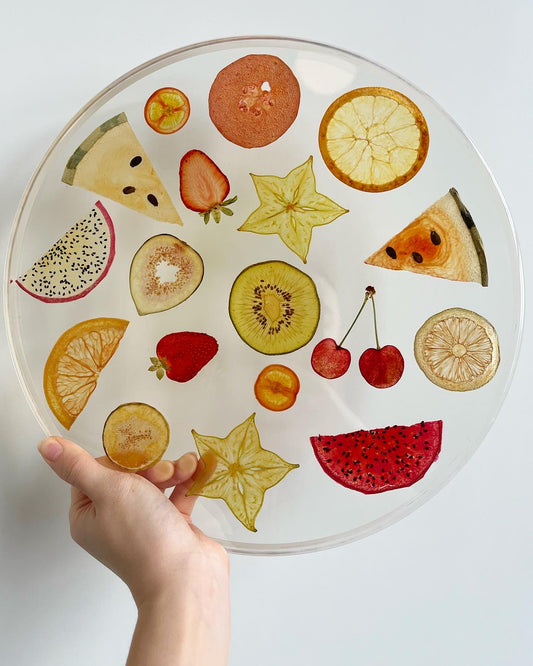 An array of fruits sit suspended in a round, transparent resin. A durable-yet-whimsical addition to your home decor. Serve cocktails, use as a vanity tray, or simply display as an incredible objet d'art.