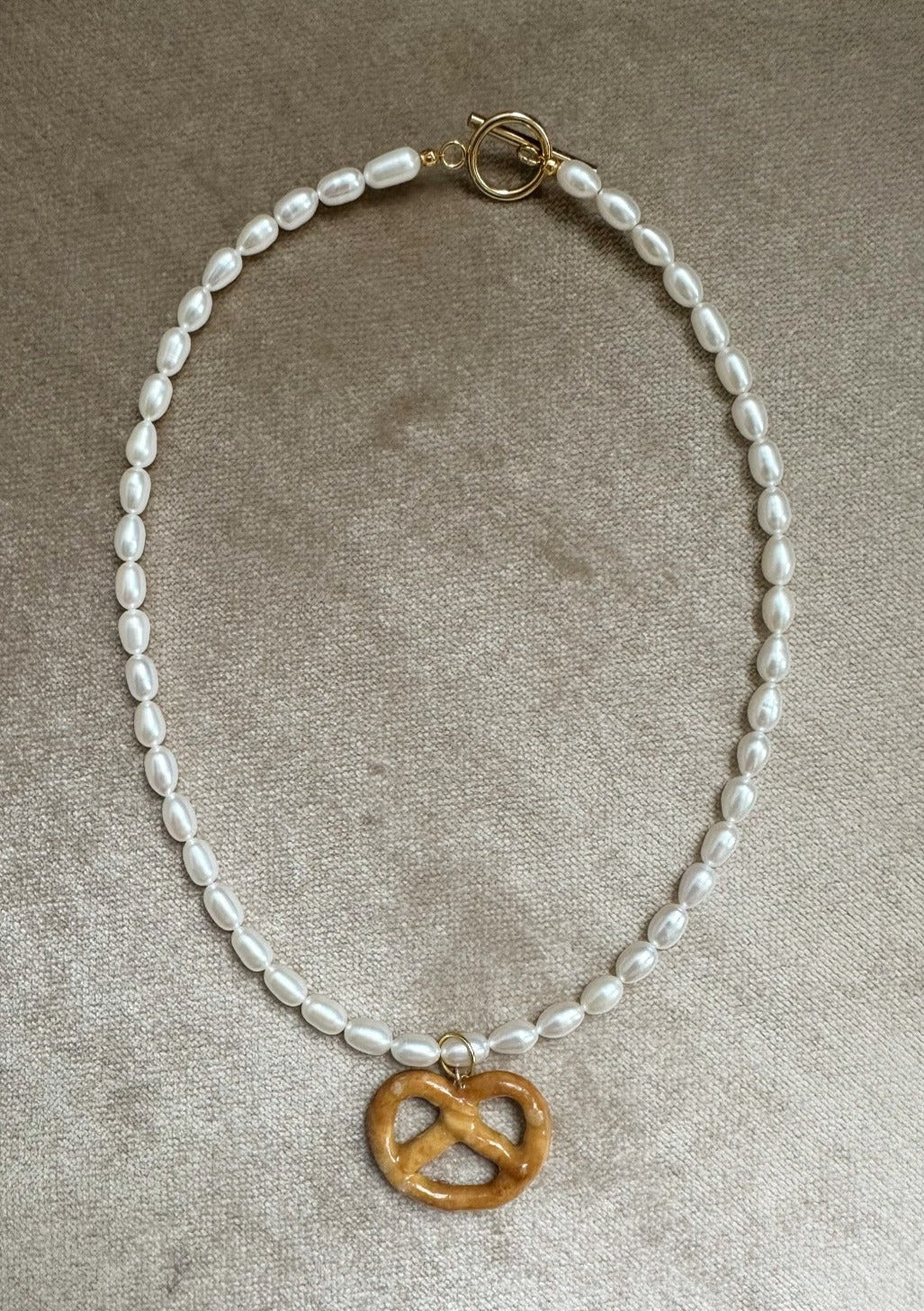 Resin coated pretzel on beaded pearl necklace with gold clasp.