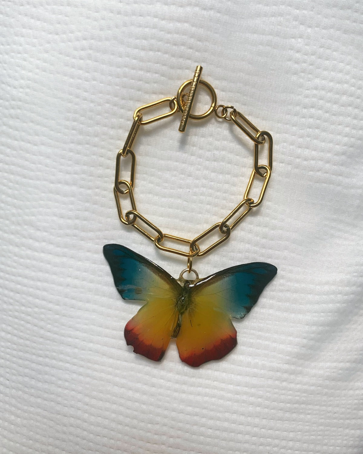 Red, Yellow, Blue, and Black Butterfly preserved in resin on gold bracelet chain.