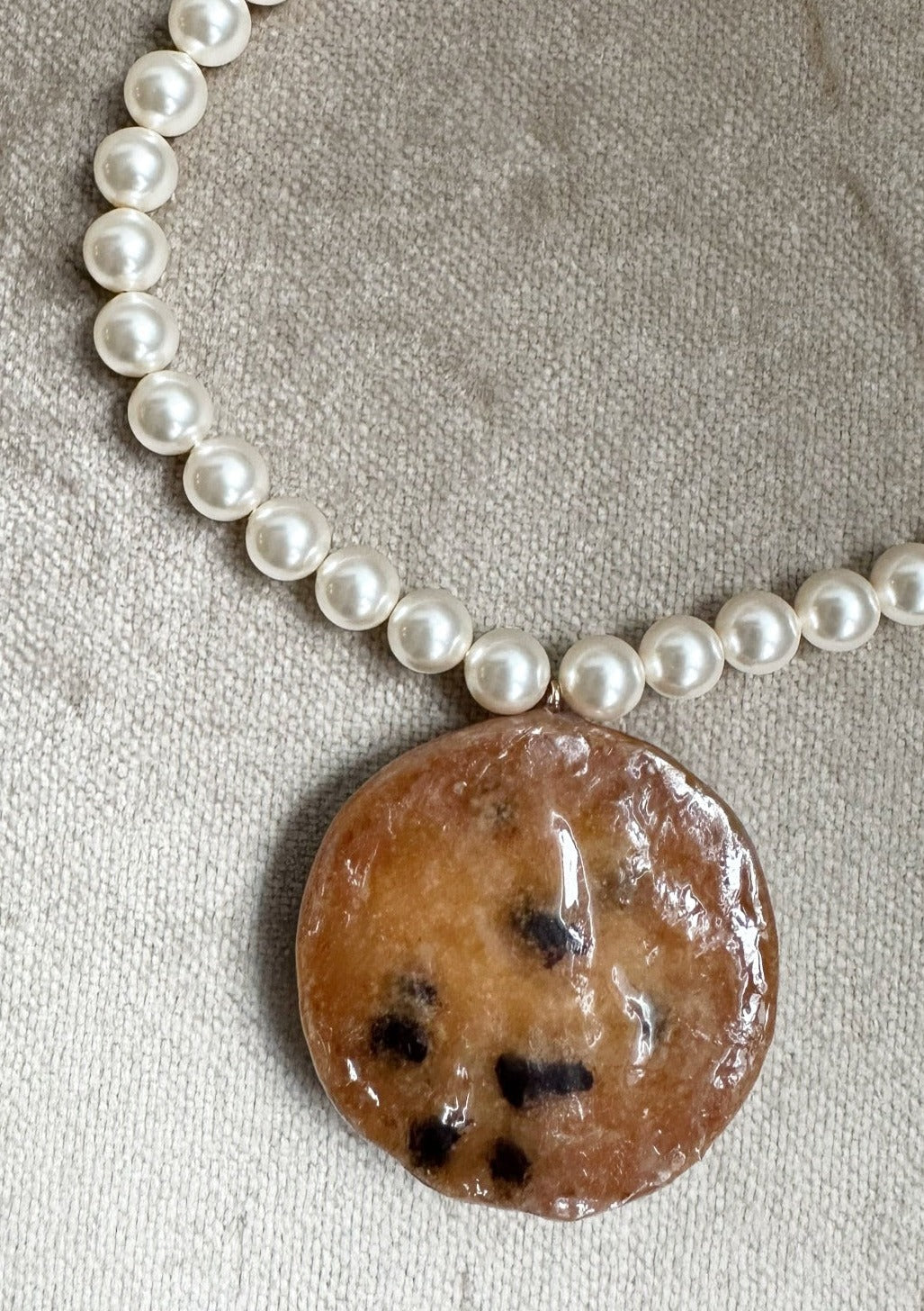 Resin coated cookie on beaded pearl necklace with gold clasp.