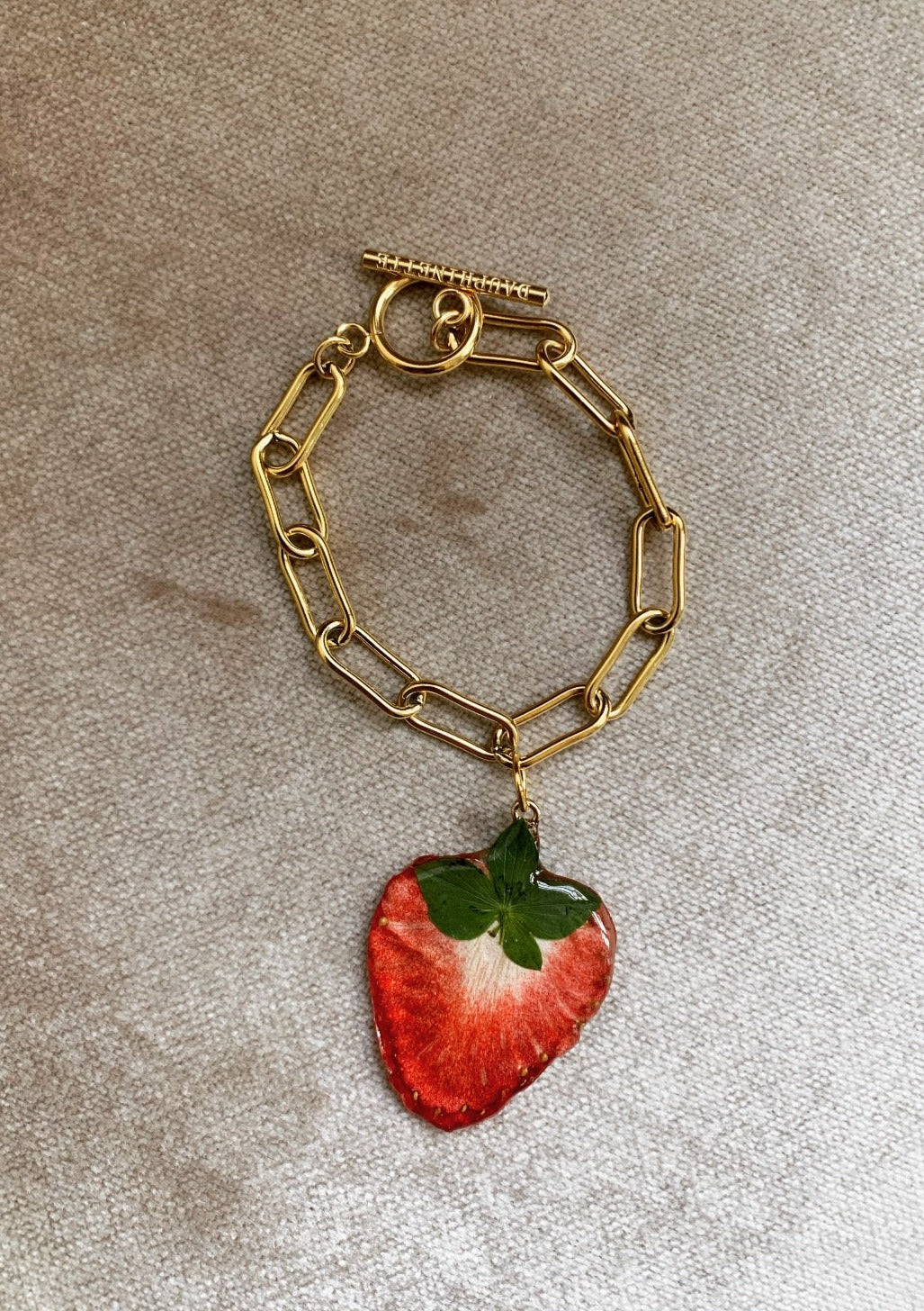 A preserved strawberry, suspended from a gold-plated stainless steel Albert chain.