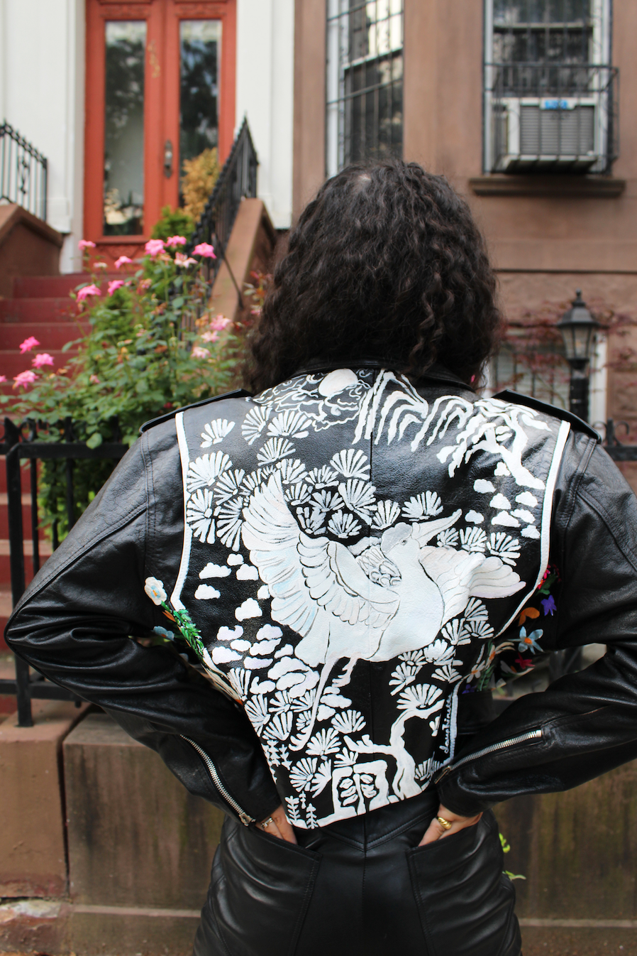 Fully hand-painted black motorcycle jacket dating from the 1980s. Floral scrapbook imagery to front, inspired by vintage pressed botanical prints. Pearl powder infused, crane-painted backside, modeled after antique mother-of-pearl inlaid cabinetry. Cropped style with silver hardware and adjustable belt