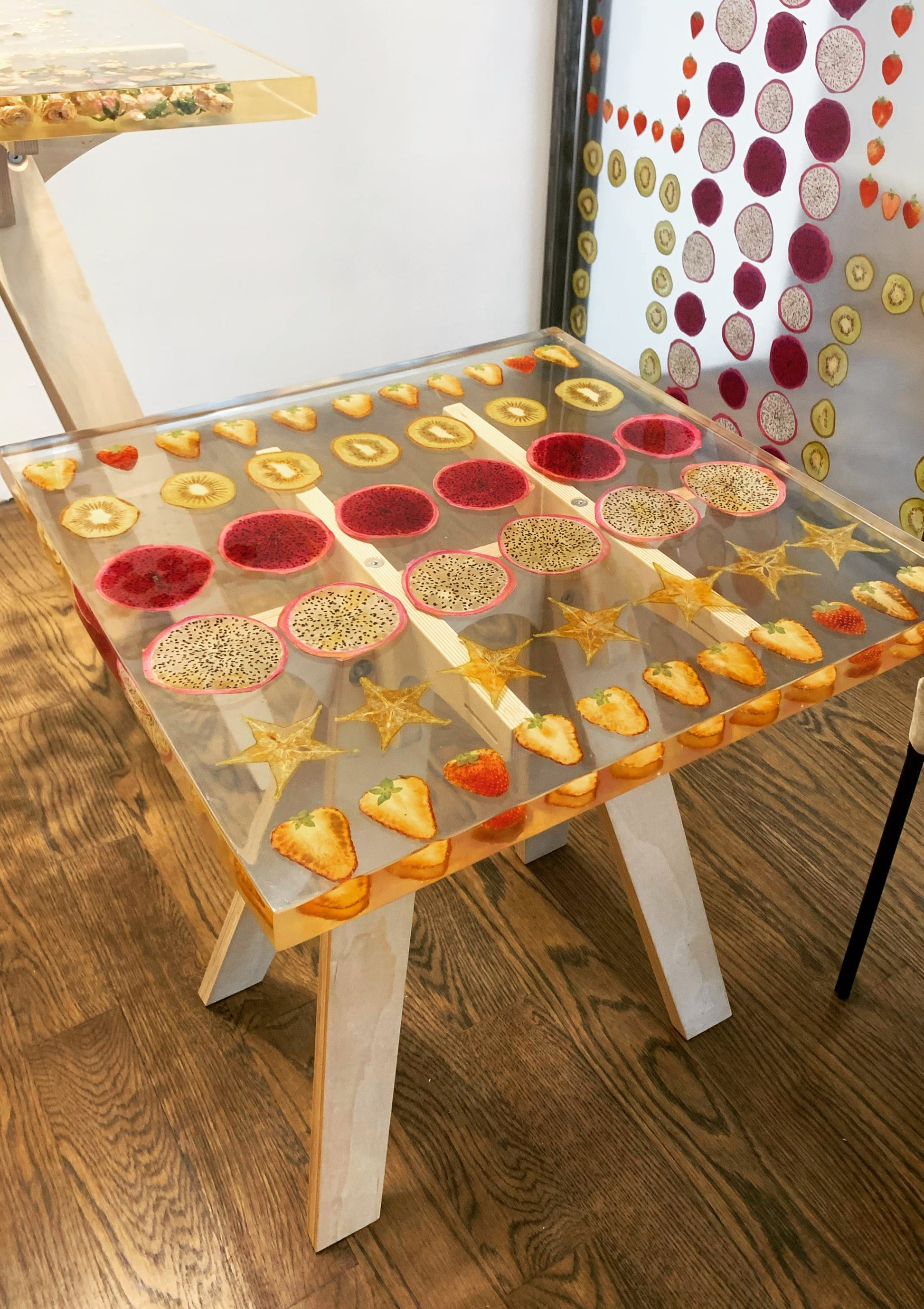 a hand-poured resin cocktail table where preserved strawberries, starfruit, kiwis, and dragonfruit float atop a sturdy birch base. 